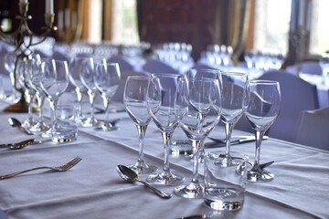 Tables setting for a festive banquet. There are glasses and cutlery on a white tablecloth