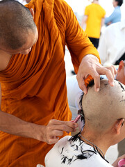 Obraz na płótnie Canvas A monk shaves the head of a young man during an ordination ceremony