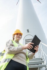 Woman in a safety vest smiling at the camera, in front of a windmill