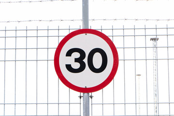 Speed limit sign attached to wire mesh fence. Maximum thirty kilometers per hour. Safety on road...