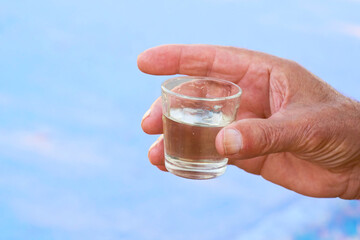 A man's hand holding a glass of vodka against a blue sky