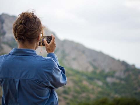 girl takes pictures of mountain landscape on her phone