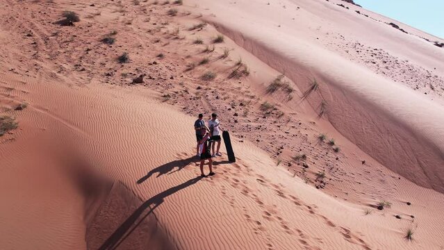 Drone view of people riding on a board on the sand dunes of the desert