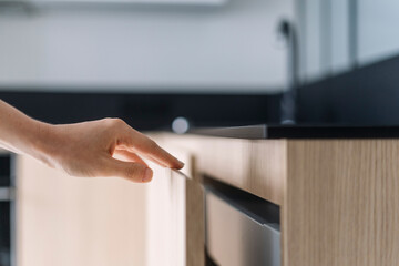 Selective focus on woman hand opening door on wooden cabinet under countertop - obrazy, fototapety, plakaty