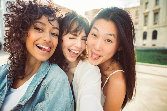Three young women taking selfie pic with smart mobile phone device outside - Multiracial women smiling at camera together