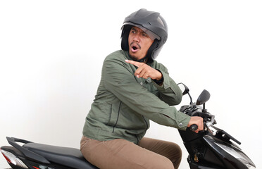 Side view of angry asian man looking behind, pointing and shouting while driving motorcycle....