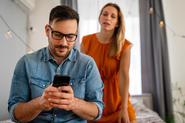 Jealous woman spying boyfriend and watching his mobile phone. Couple cheating jealousy concept