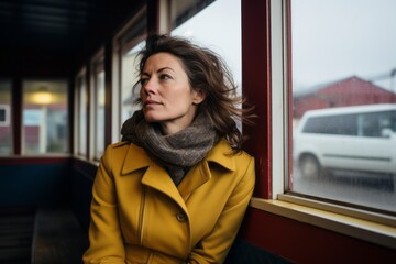 Portrait of a young woman in yellow coat and scarf near the window of a train station.