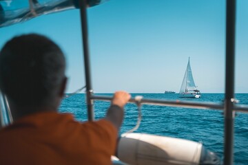 Silhouette of a person gazing from a yacht on a vast ocean with boats visible in the distance
