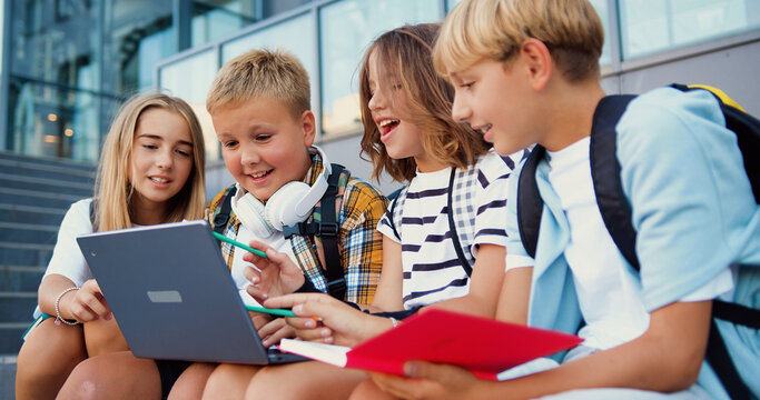 Group of diverse good-looking modern school girls and boys doing a project together with a laptop in a school building background. Concept of learning and lifestyle in teens life.
