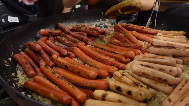 Street food hot dog - grilled German or Bavarian Nuremberg sausages with cabbage sauerkraut on a huge pan bowl at market.