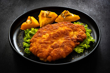 Crispy breaded seared chicken cutlet with baked pumpkin  on wooden table
