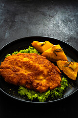 Crispy breaded seared chicken cutlet with baked pumpkin  on wooden table
