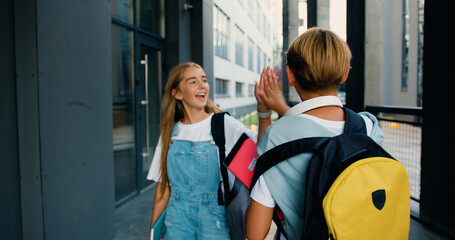 School boy child with backpack alone going running to modern school building a classmate going to meeting girl says hello and gives a high five © serg