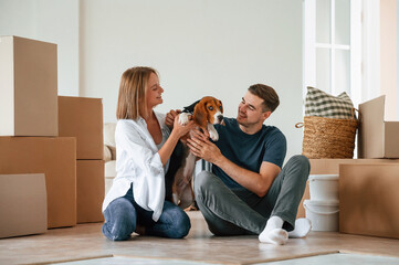 Sitting and playing with dog. Young couple are moving to new home