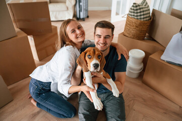 Sitting and smiling. Young couple with dog are moving to new home
