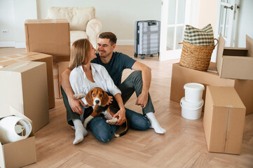 Conception of success. Sitting on the floor. Young couple with dog are moving to new home