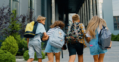 Rear view. Good-looking school child friends climb stairs going to class with backpacks. Boys and girls high school students having fun after school. They are smiling and having fun.