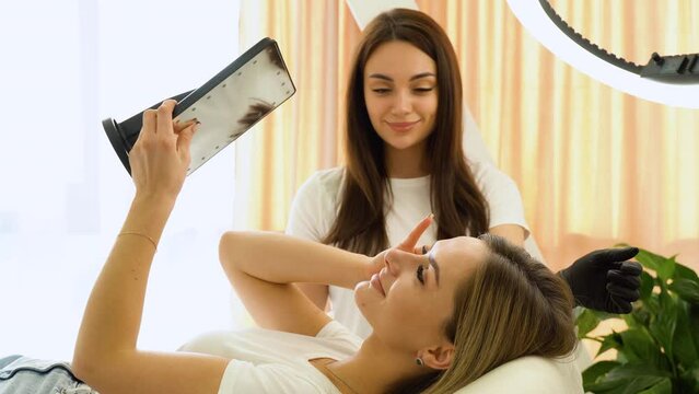Beautiful young woman looks at herself in the mirror in the beauty salon after the procedure permanent make up of lips and eyebrows