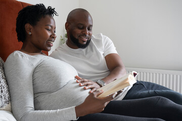Smiling man touching pregnant woman's belly on bed