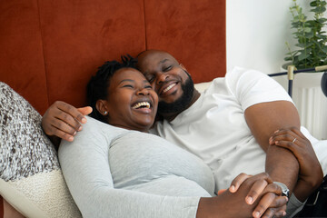 Smiling man embracing pregnant woman on bed - obrazy, fototapety, plakaty