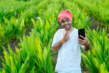 Young indian farmer showing debit or credit card at his green agriculture field, using mobile phone