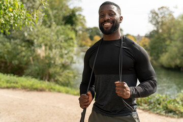 Portrait of smiling athletic man with jump rope in park