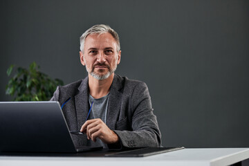 Portrait of a serious-looking mature businessman, looking at the camera while working in his office, online.