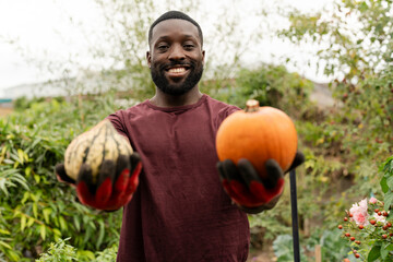 Portrait of smiling man holding pumpkins in urban garden