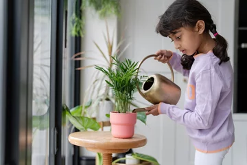 Tuinposter Little girl watering plant at home © Cultura Creative