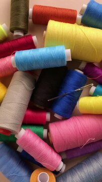 Many colorful spools with thread and needle for sewing, rotating motion, vertical video
