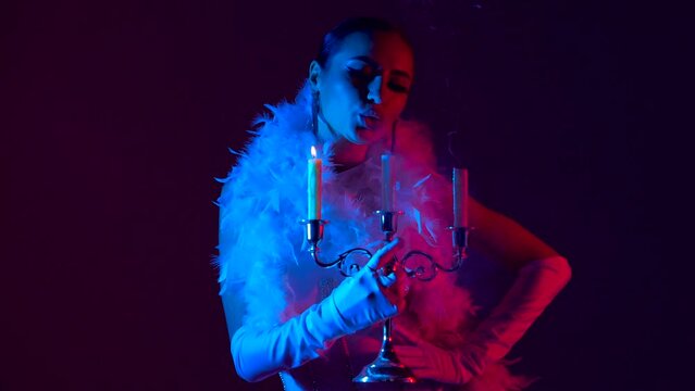 Beautiful and sexy dancer posing for camera with a candelabra under blue and purple-colored lights