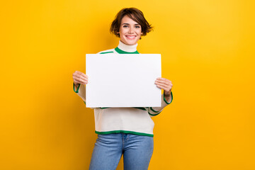 Photo cheerful young positive girl smile marketer hold paper placard empty space blank advertiser isolated on yellow color background - obrazy, fototapety, plakaty