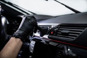 Car wash employee or a car detailing studio worker carefully cleans the air vents inside a car with...