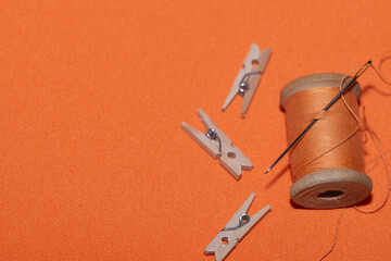 vintage threads on wooden spools and needle  of orange color against a light terracotta background.