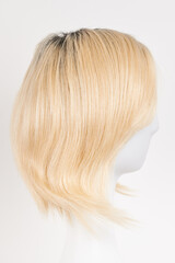 Natural looking blonde fair wig on white mannequin head. Short hair cut on the plastic wig holder isolated on white background, side view.