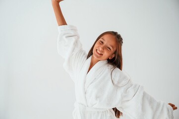 Young female kid is standing against white background