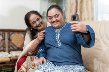 Woman and down syndrome granddaughter taking selfie in living room - obrazy, fototapety, plakaty
