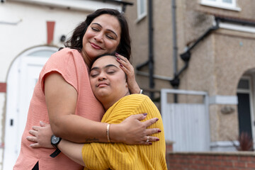 Portrait of woman embracing down syndrome daughter in front of house