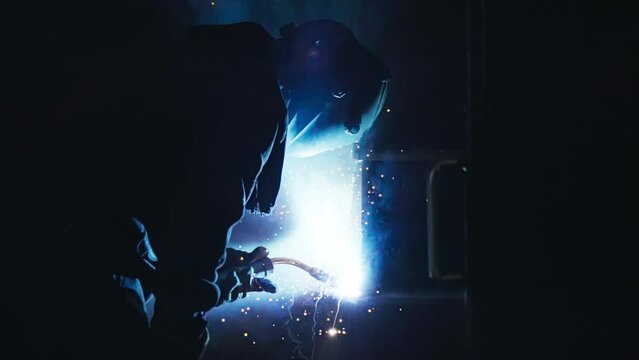 Worker using the welding torch at the industrial metalworking facility. Worker producing metalworking items at the industrial factory. Worker welding details to make industrial metalworking products