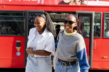 Smiling young women getting off city bus - obrazy, fototapety, plakaty