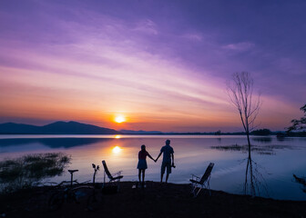 Photo silhouette scene, man, woman, travel couple stand and holding hands watch sunset at last light on New Year's Eve, enjoy relax in vacation. Romantic on holiday at lake in Huai Mai Teng, Thailand