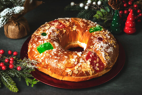 Roscon de reyes with cream and christmas ornaments on a red plate. Kings day concept spanish three kings cake.Typical spanish dessert for Christmas