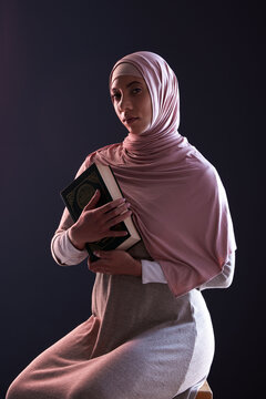Quran, religion and portrait of a muslim woman in a studio with traditional clothes and hijab. Serious, faith and young islamic female person with the holy Arabic book isolated by a black background.