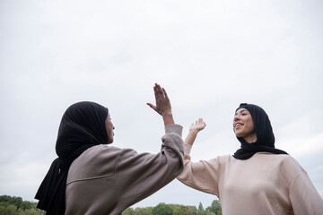 Two smiling women in hijabs giving high five outdoors