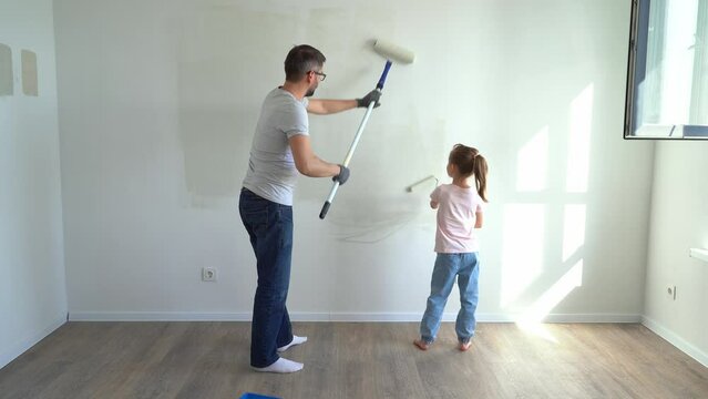 Back view father and little daughter paint wall with rollers at home. Family make renovations in new apartment. Repair concept