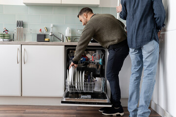 Male couple unloading dishwasher at home - obrazy, fototapety, plakaty