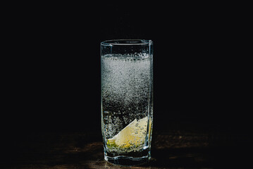 Gin tonic cocktail with lime slice in a glass splash on black background