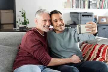 Smiling male couple taking selfie on sofa