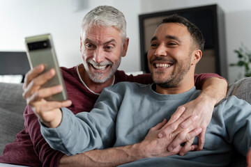 Smiling male couple taking selfie on sofa